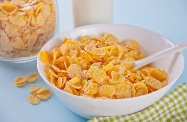 A bowl of dry corn flakes cereal on blue background