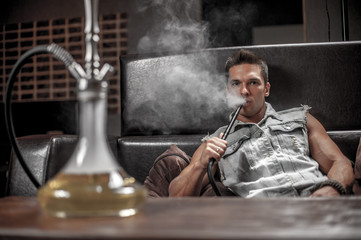 Sexy young man enjoy aromatic shisha in the hookah bar.
