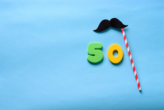 50 celebrating yellow green number with  mustache cute paper mask on straw stick.Fifty Modern alphabet digits on blue background. 50 th birthday party anniversary card.Flat lay, top view.Copy space