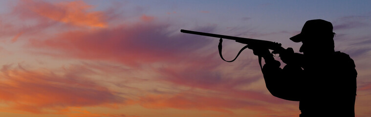 Silhouette of a hunter with a gun in the reeds against the sun, an ambush for ducks with dogs