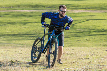 Fototapeta premium Cyclist in shorts and jersey on a modern carbon hardtail bike with an air suspension fork rides off-road on green hills near the forest 