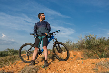 Obraz premium Cyclist in shorts and jersey on a modern carbon hardtail bike with an air suspension fork rides off-road on the orange-red hills at sunset evening in summer
