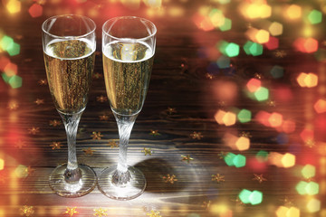 Two glasses of champagne on wooden table in New Year's Eve with bright glitter
