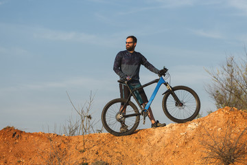 Plakat Cyclist in shorts and jersey on a modern carbon hardtail bike with an air suspension fork rides off-road on the orange-red hills at sunset evening in summer