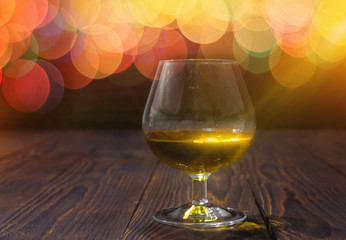 Glass of whiskey or brandy on wooden table on bright glowing background