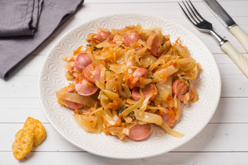 Stewed cabbage with sausages in a plate on the table. Selective focus.