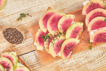 Healthy breakfast toasts from sliced watermelon radish or chinese daikon, chia and cottage cheese on board wooden background. Top view. Flat lay. Copy space.