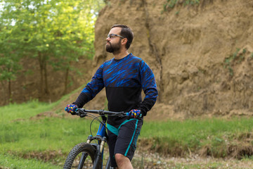 Fototapeta premium Cyclist in shorts and jersey on a modern carbon hardtail bike with an air suspension fork rides off-road on green hills near the forest 