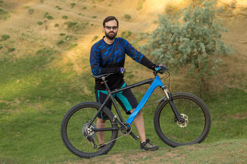 Fototapeta na wymiar Cyclist in shorts and jersey on a modern carbon hardtail bike with an air suspension fork rides off-road on green hills near the forest 