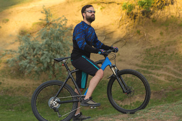 Fototapeta premium Cyclist in shorts and jersey on a modern carbon hardtail bike with an air suspension fork rides off-road on green hills near the forest 