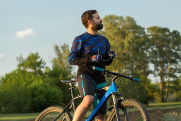Fototapeta premium Cyclist in shorts and jersey on a modern carbon hardtail bike with an air suspension fork rides off-road on green hills near the forest 