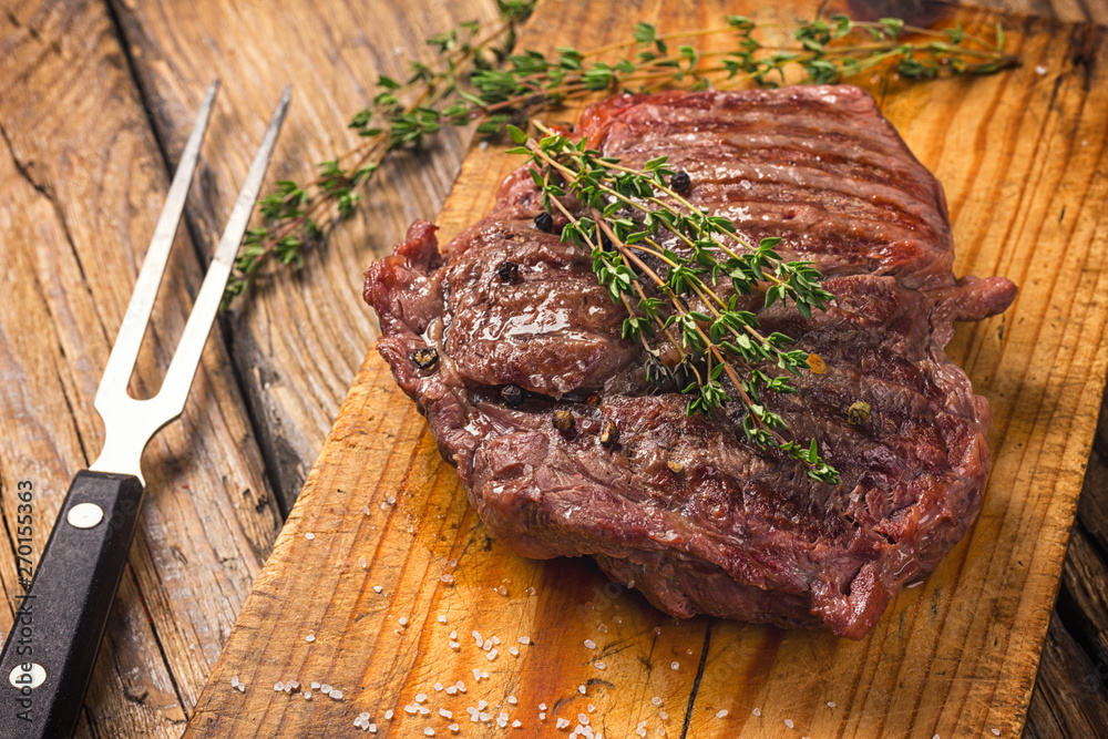 Sticker juicy medium rare beef steak on wooden board with herbs spices and salt.