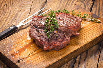 Juicy medium rare beef steak on wooden board with herbs spices and salt.