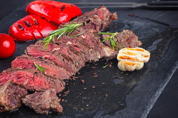 Juicy medium rare beef steak slices on ceramic board with herbs spices and salt.
