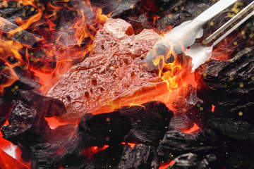 raw marbled beef steak with coals and smoke