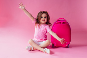 Portrait of little traveler girl on travel case with hat photo camera and passport ticet on pinc studio