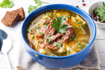 Russian traditional cabbage soup with meat and fresh herbs on a light table.
