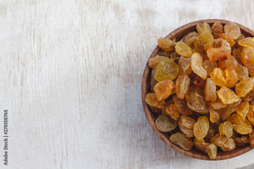 Sticker Light yellow raisins in a wooden bowl on a light white background. Close-up. Isolated.