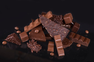 Broken chocolate pieces and cocoa powder on wooden background.