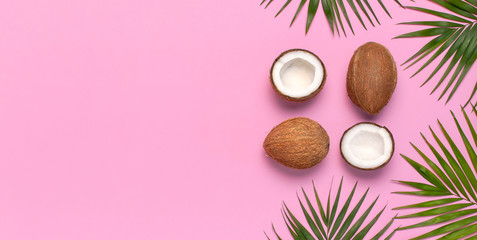 Tropical leaves and fresh coconut on pink background. Flat lay, top view, copy space. Summer background, nature. Healthy cooking. Creative healthy food concept, half of coconut