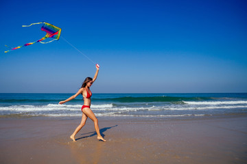 happy brunette girl in a bathing suit and short pink playing with flying kite on tropical beach copyspase hills and mountains background