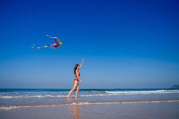 happy brunette girl in a bathing suit and short pink playing with flying kite on tropical beach copyspase hills and mountains background