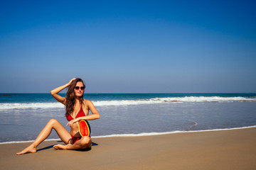 Fototapeta na wymiar Beautiful young female in swimsuit and red sunglassses hold slice of watermelon red while standing on beach detox