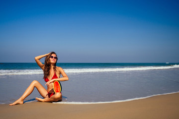 Beautiful young female in swimsuit and red sunglassses hold slice of watermelon red while standing on beach detox