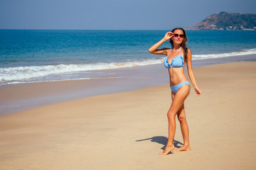 beautiful tanned female fitness big boobs model in a fashion stylish swimsuit on sea ocean beach blue sky and palm trees background.summer vacation