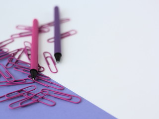 Fototapeta premium Closeup of purple stationery. Pens and paperclips on white and purple backgrund.