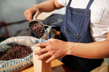 Close-up of man packing coffee beans from shovel into the coffee bag while working on coffee factory