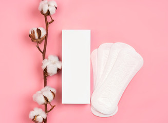 White packaging of sanitary pads with cotton flowers on pink background. Concept of critical days, menstruation