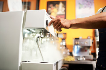 Close-up of waiter standing near the coffee machine and making hot espresso in cafe