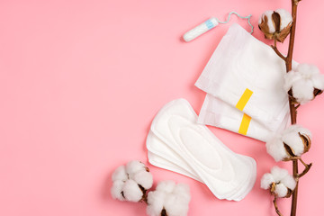 Menstrual napkins and tampons with cotton flowers on pink background. Concept of critical days, menstruation
