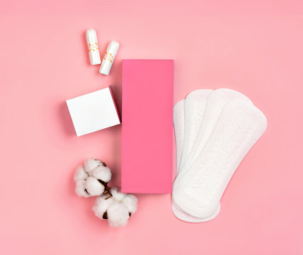 Packaging of sanitary pads and packaging of tampons with cotton flowers on pink background. Concept of critical days, menstruation