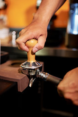 Close-up of male barmen using grinder to grinding coffee into powder at the restaurant