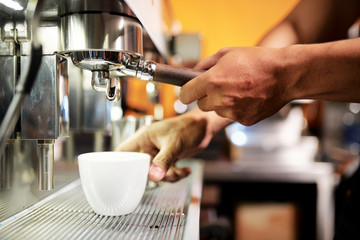 Close-up of male hands putting the cup under the crane of coffee machine and making hot coffee for client in coffee shop