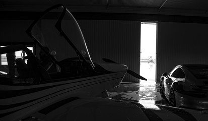 propeller plane with sport car in a hangar at an airfield. rich life - obrazy, fototapety, plakaty
