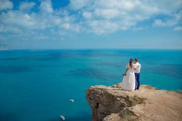 Fototapeta na wymiar Beautiful couple on the sea rocks in wedding dress. Just married view from behind.