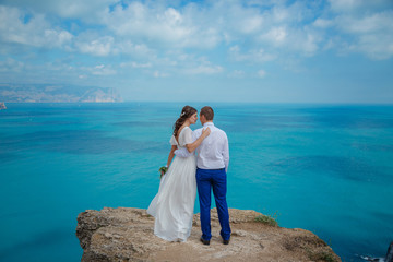 Beautiful couple on the sea rocks in wedding dress. Just married view from behind.