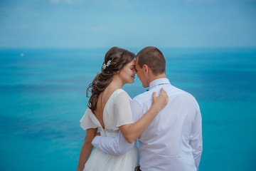 Beautiful couple on the sea rocks in wedding dress. Just married view from behind.