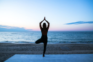 woman doing yoga at sunrise on the sea, silhouette of yoga poses