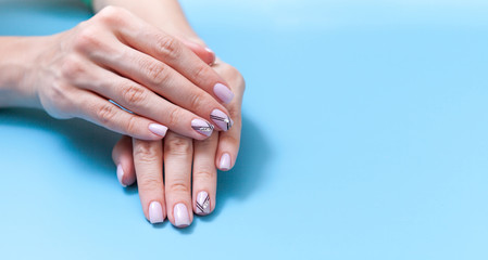 Tender hands with perfect nude manicure on trendy pastel blue background. concept of healthy and beautiful hands.