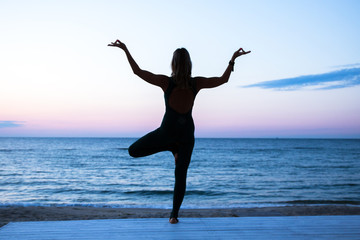 Fototapeta na wymiar woman doing yoga at sunrise on the sea, silhouette of yoga poses