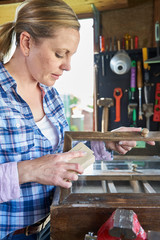 Mature Woman Upcycling Furniture In Workshop At Home