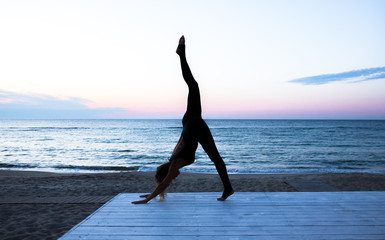 unrecognizable woman doing yoga at sunrise on the sea, silhouette of yoga poses