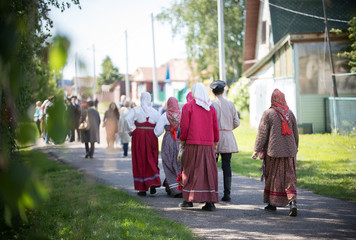 People in traditional Russian clothes walk between wooden houses