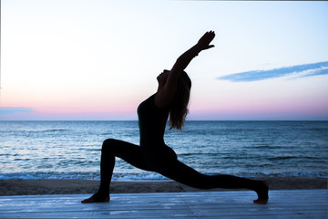 unrecognizable woman with beautiful body doing yoga at sunrise on the sea, silhouette of yoga poses