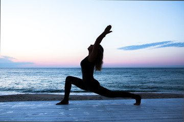 unrecognizable woman with beautiful body doing yoga at sunrise on the sea, silhouette of yoga poses