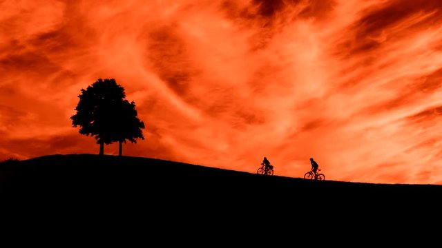Two cyclists climb the hill. Sunset. Romantic picture.